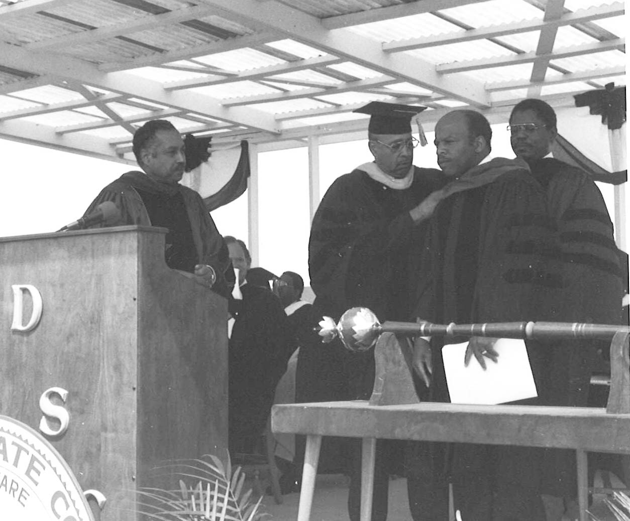 Dr. Ulysses S. Washington and Henry Tisdale place the honorary doctoral sash on John Lewis. Dr. William B. Delaware watches.