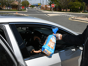 A Food Pantry hands a student a loaf of bread while another volunteer puts a box of food in her back seat.