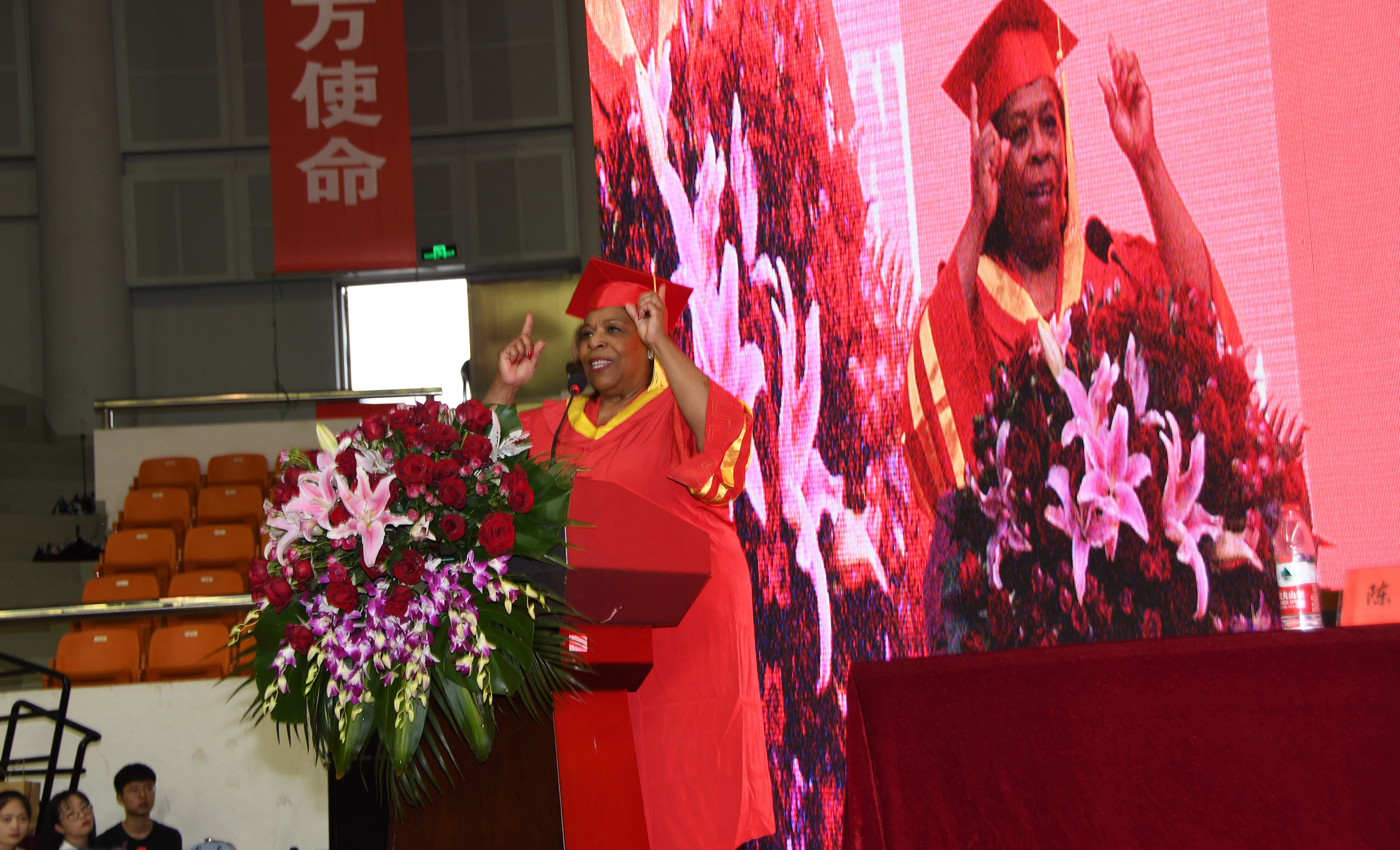 Dr. Wilma Mishoe gives her Commencement address while a larger-than-life image of her lights up the stage behind her.