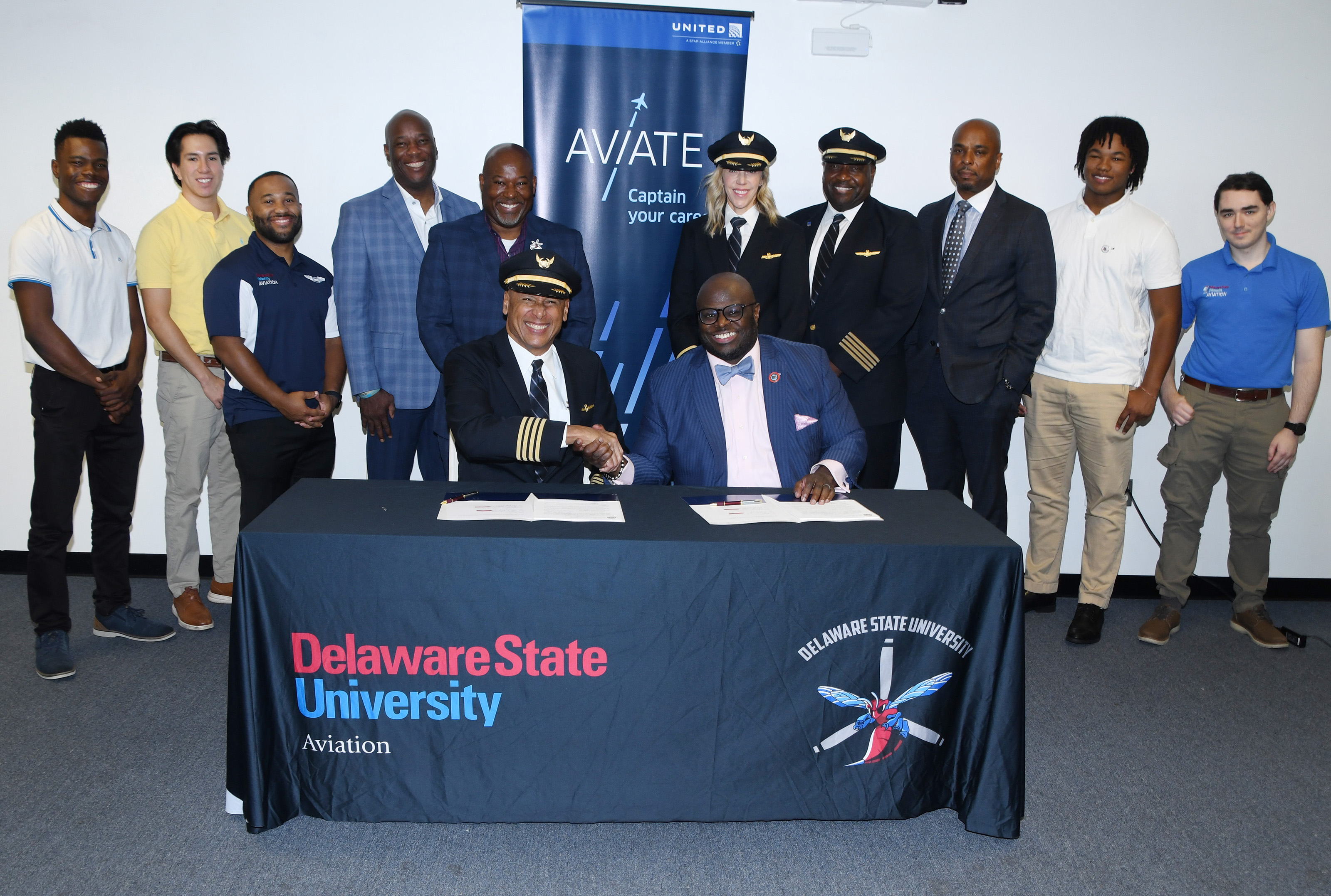 (Seated l-r) United Airlines' Capt. Mike Bonner and University President Tony Allen shake hands after signing the agreement.