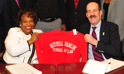 Dr. Wilma Mishoe receives a Mitchell Hamline shirt from its president, Mark C. Gordon.