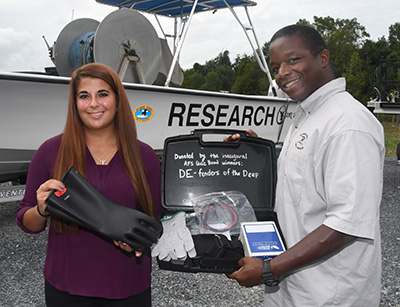 Angelina Watts presents the fishing gloves to Johnny Moore, an environmental scientist who accepted them for DNREC.