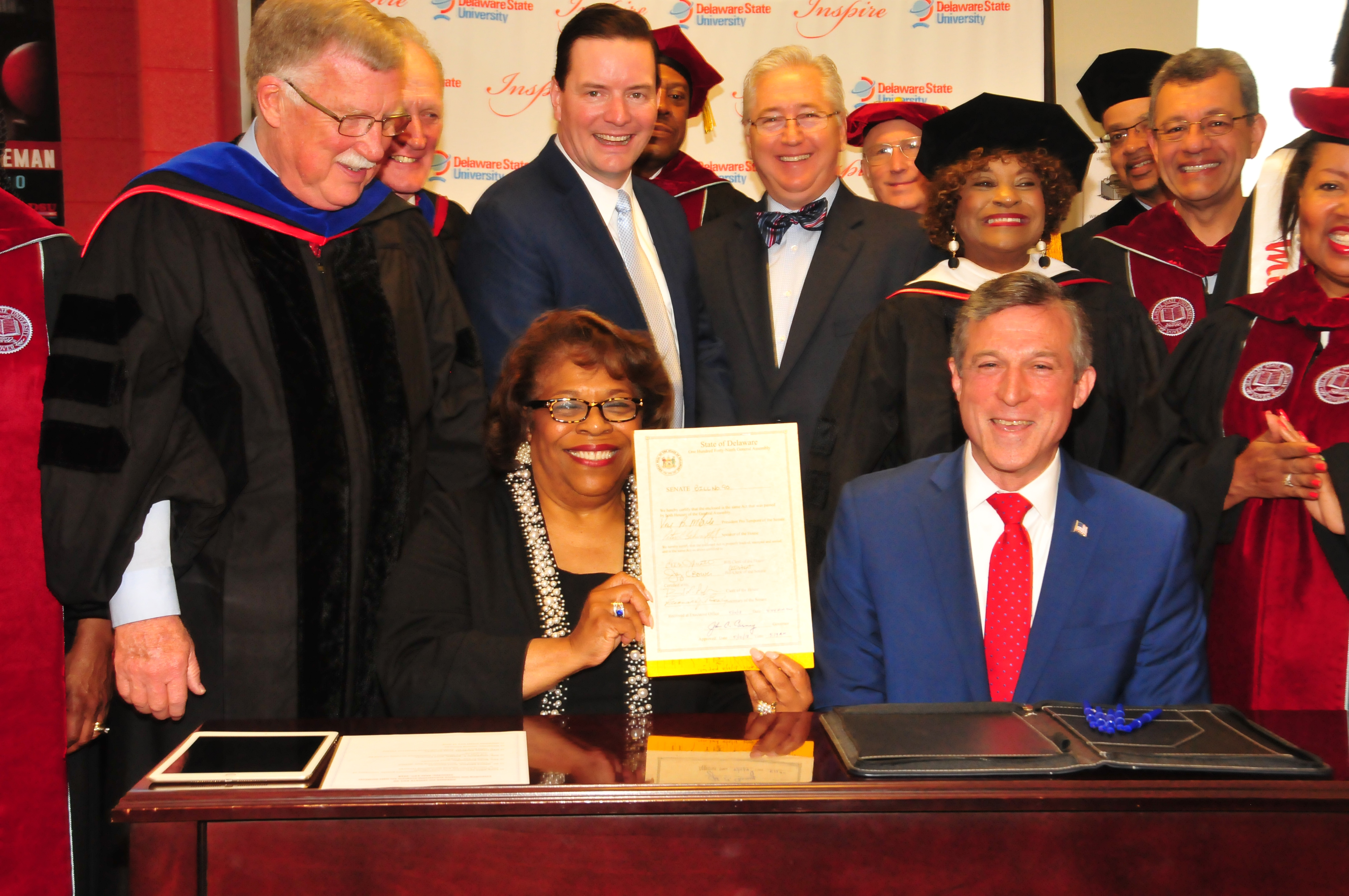 Interim DSU President Wilma Mishoe holds the legislation just signed May 12 by Gov. John Carney (seated next to her) that adds a fourth year of state funding to the Inspire Scholarship Program. 