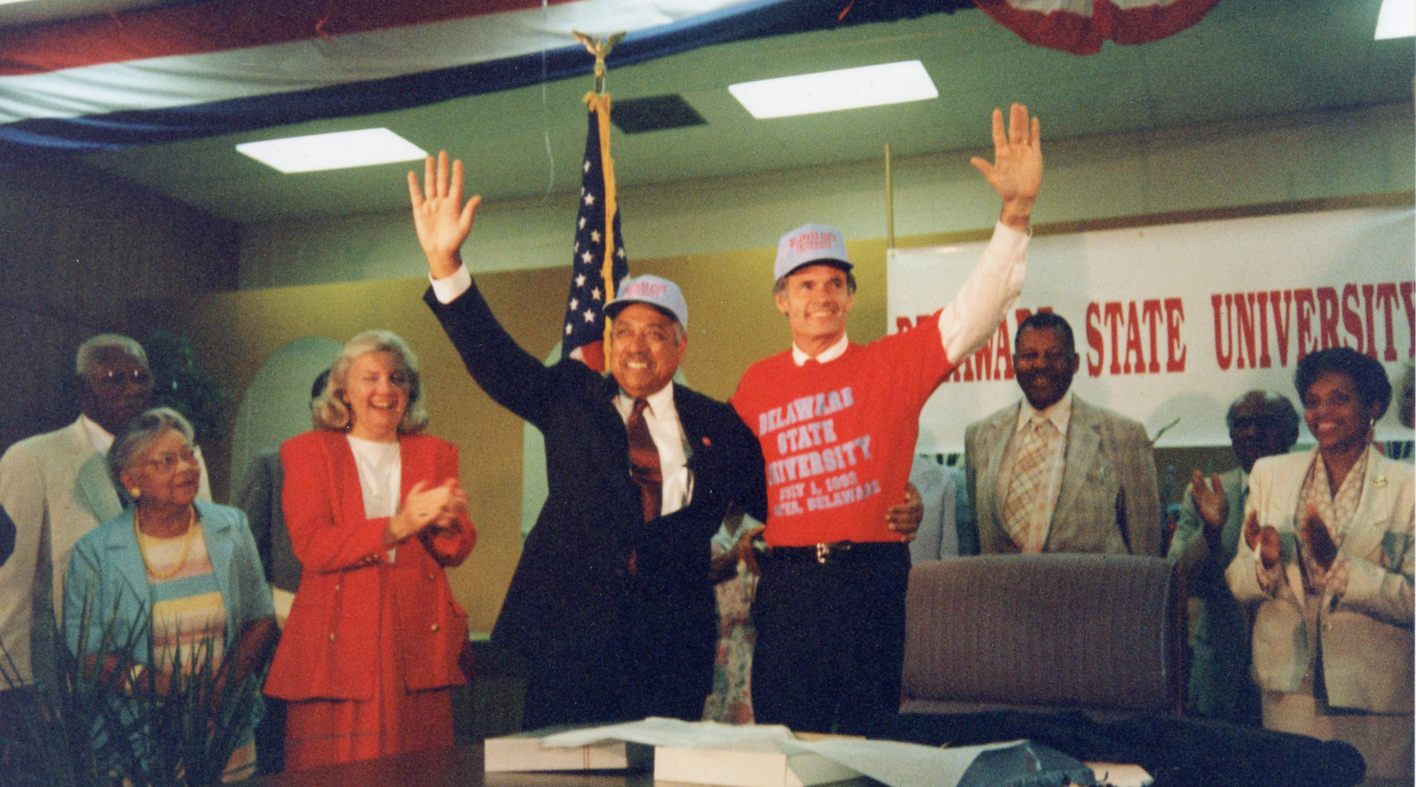 On July 1, 1993, William B. DeLauder, president of Delaware State University, waves with Gov. Tom Carper at the signing of Senate Bill 138 which changed Delaware State College to Delaware State University. Looking on in the background, from left, are Senator Herman Holloway Sr., Hattie Mishoe, Representative Nancy Wagner, James C. Hardcastle and Vermell DeLauder.