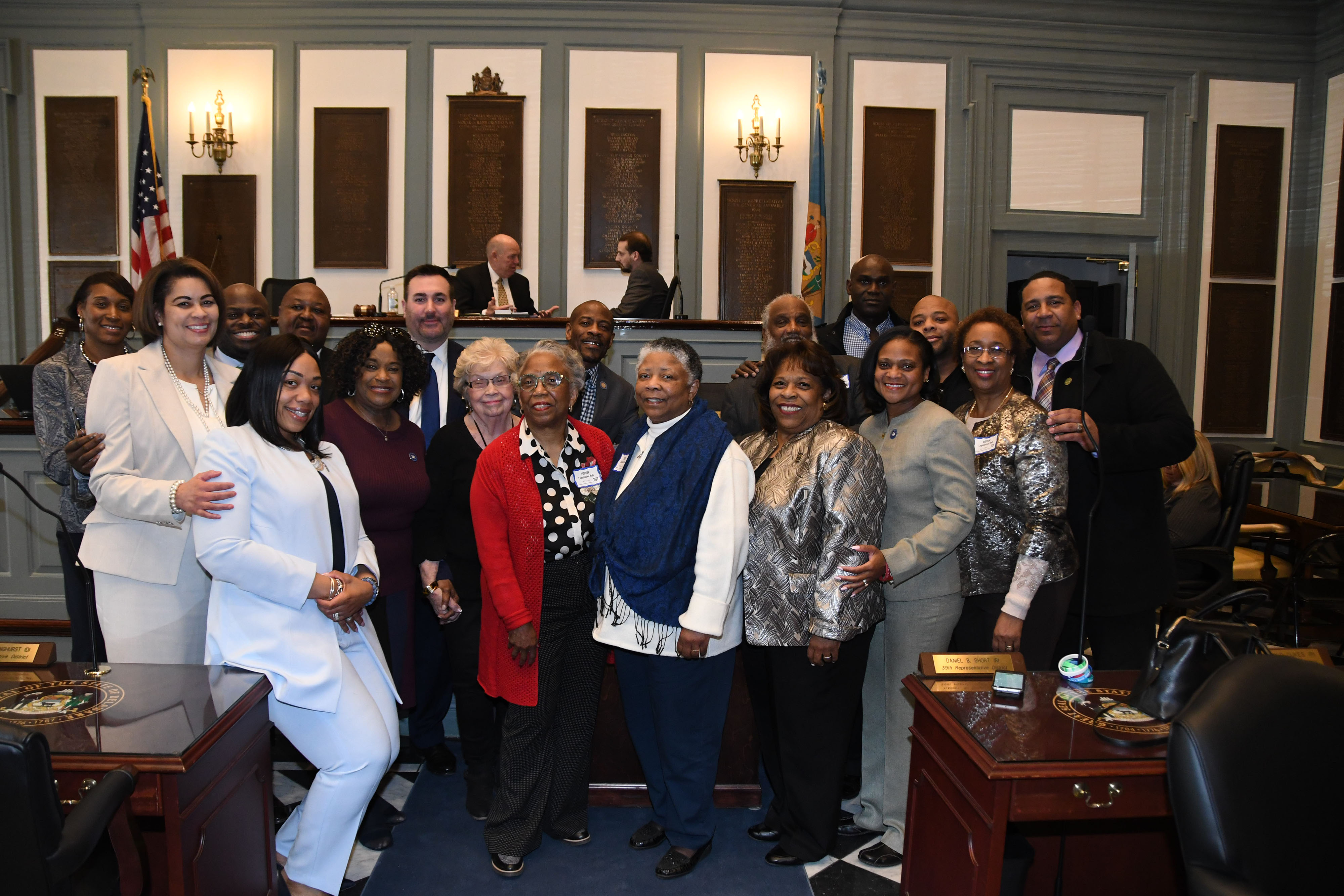 The family of Hattie Mishoe (which include her daughters Bernellyn Carey in the center in red, and to her right Rev. Rita Paige and University President Wilma Mishoe) along with some of the House Joint Resolution No. 2 sponsors and friends celebrate the legislative expression honoring the former First Lady and the wife of then-Delaware State College President Luna I. Mishoe. 