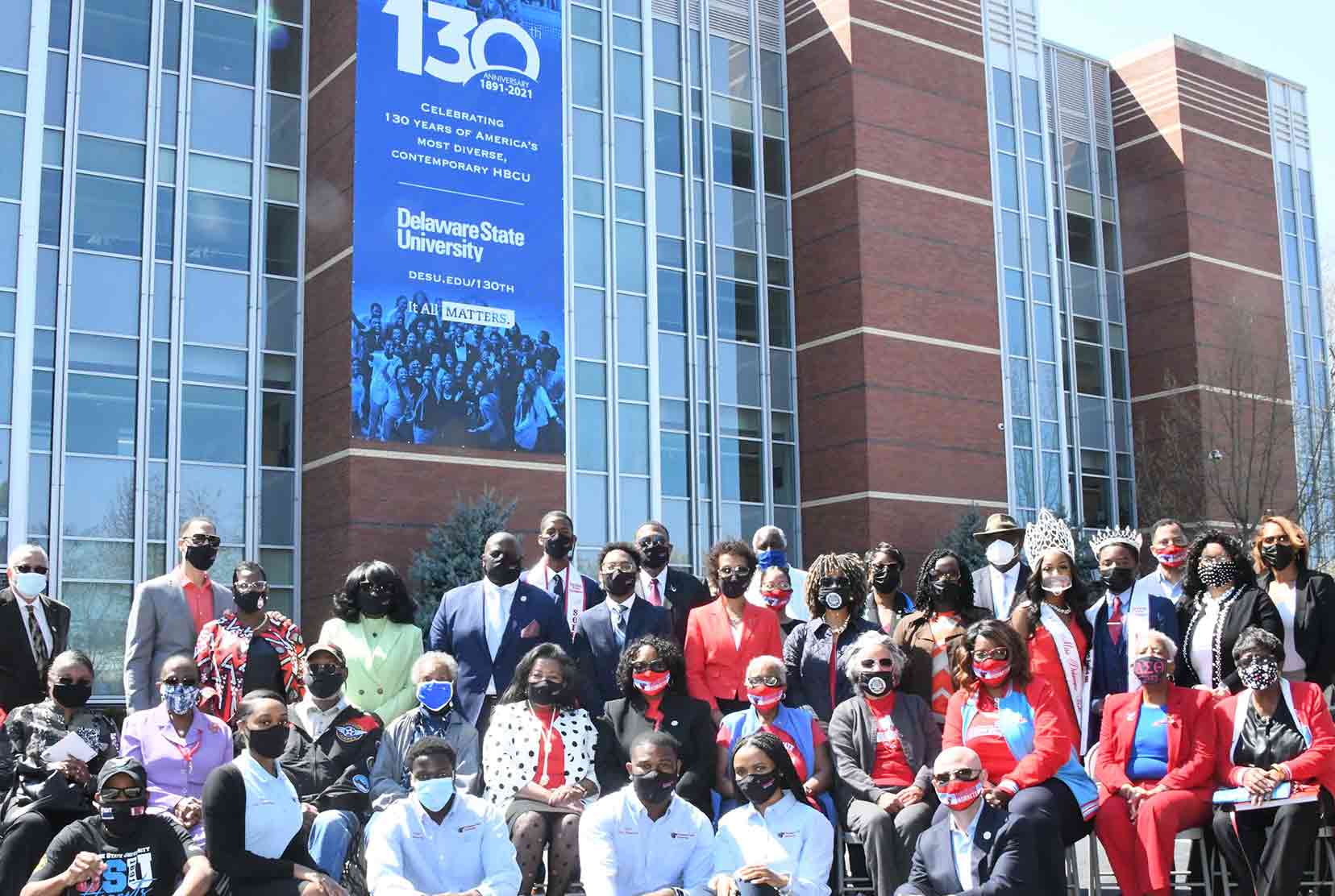 A group of Del State alumni, students, administrators and staff poses in front of the newly hung 130th Anniversary banner on the Claiborne Smith Administration Building on campus.