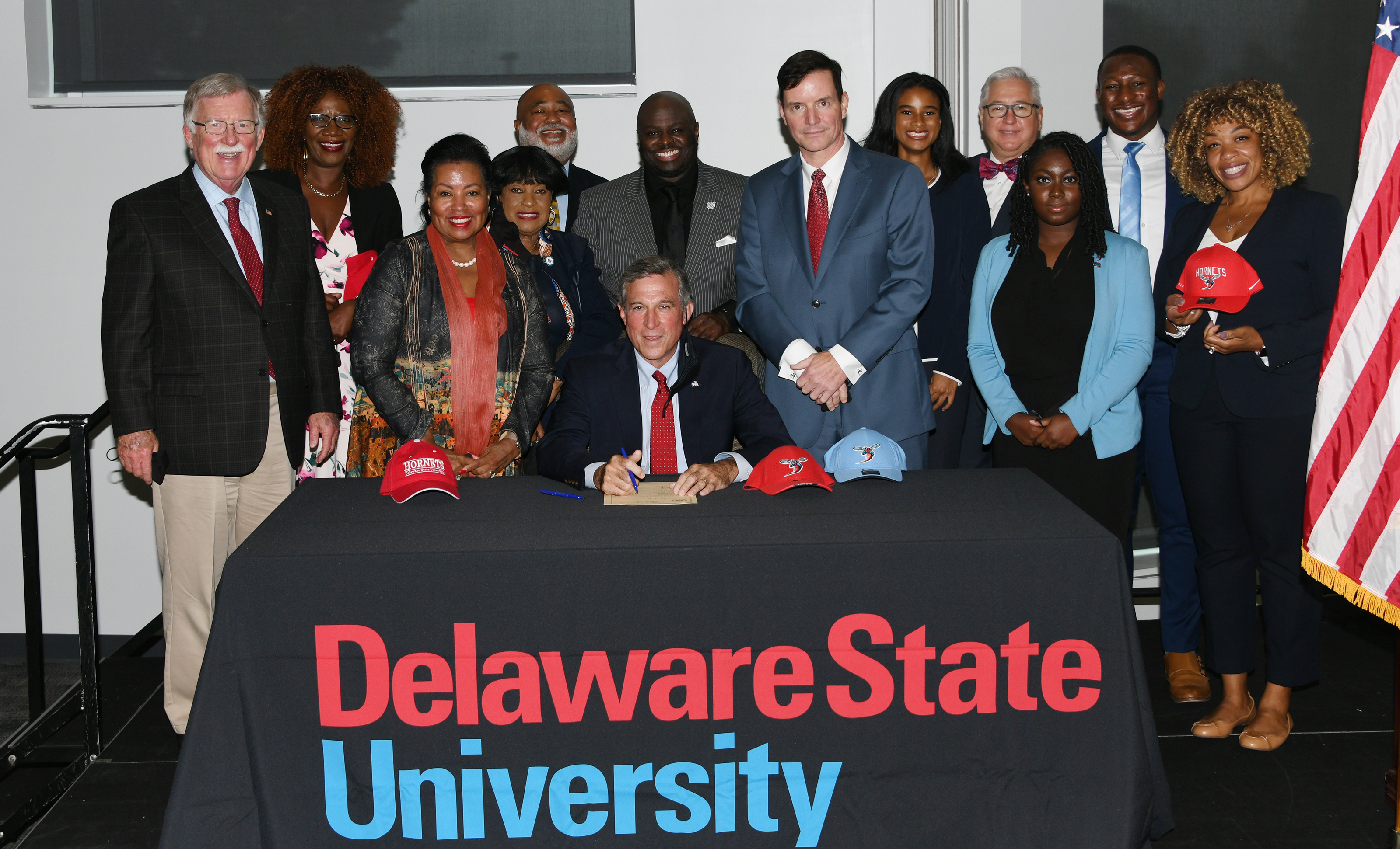 Gov. John Carney, surrounded by past and present legislators and Delaware State University administrator and student, prepares to sign Senate Bill 95. Enacted, the legislation expands the state-funded Inspire financial support into a full scholarship for qualified Delaware high school graduates.