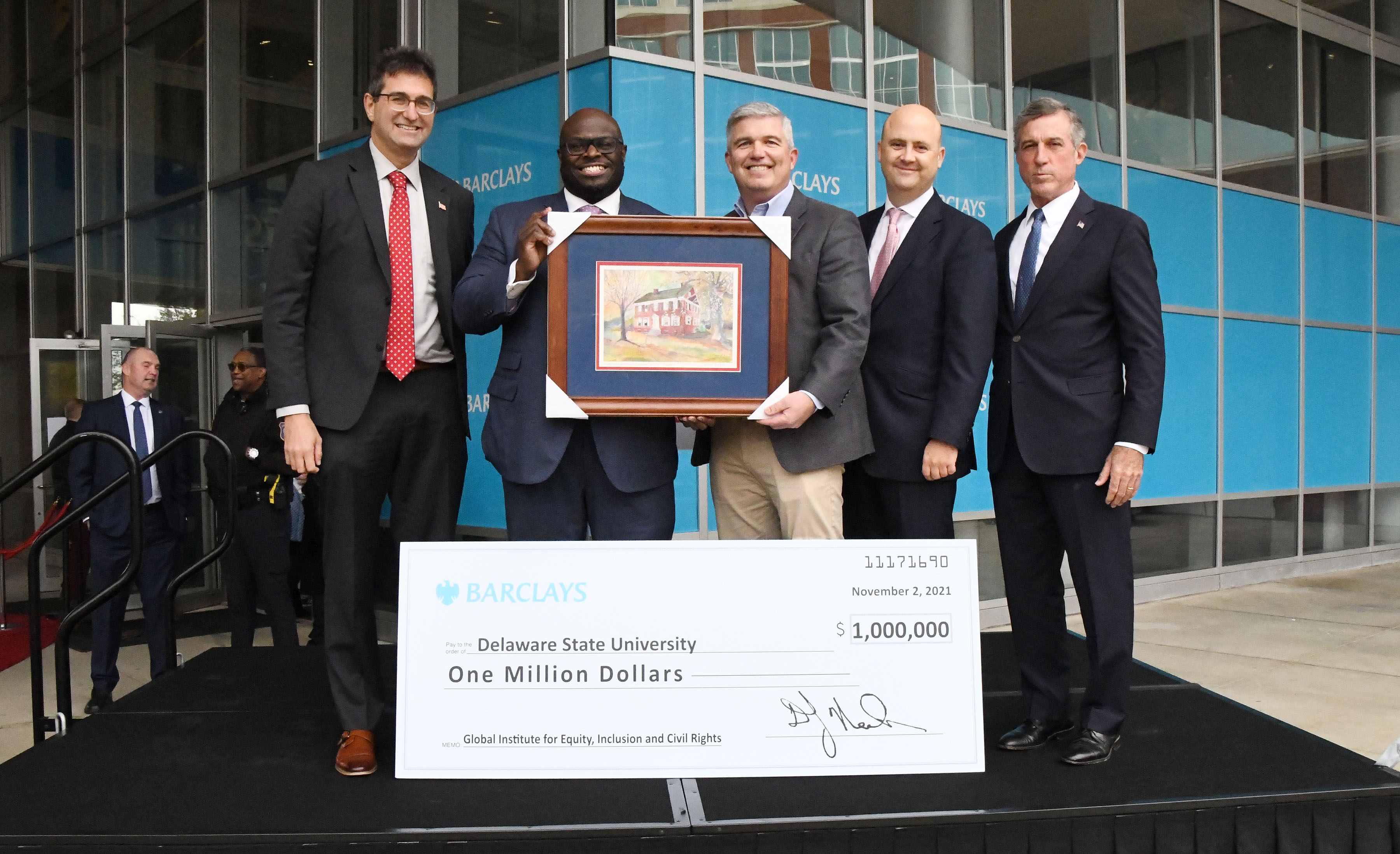 New Castle County Executive Matt Meyers, University President Tony Allen, Barclays US Consumer Bank CEO Denny Nealon, Barclays Americas CEO Richard Haworth, and Del Gov. John Carney pose with a Del State gift to Mr. Nealon and the display check symbolizing the corporation's $1M donation in support of the University's Global Institute for Equity, Inclusion and Civil Rights.