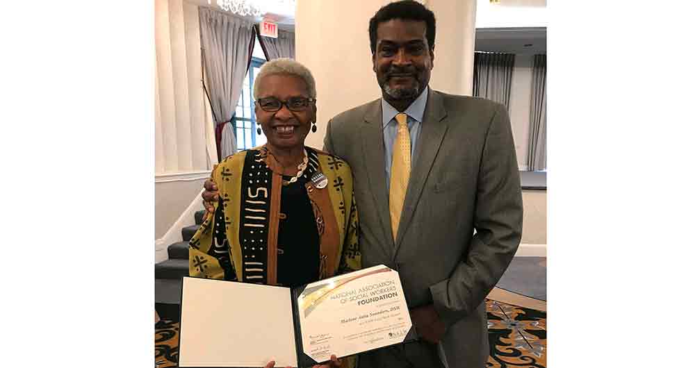 Longtime Department of Social Work faculty member Dr. Marlene Saunders shows off her Social Work Pioneer honor presented recently to her by the National Association of Social Workers. Standing alongside her is the presenter Angelo McClain, CEO of the NASW.