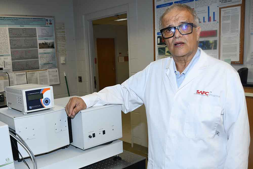 Dr. Aristides Marcano, Professor of Physics and Engineering, explains his singlet oxygen research as he stands next to a high sensitivity time-resolved spectrometer that is based on photon counting techniques. DSU's possession of such research technology assisted greatly in enabling Dr. Marcano to obtain the grant award. 