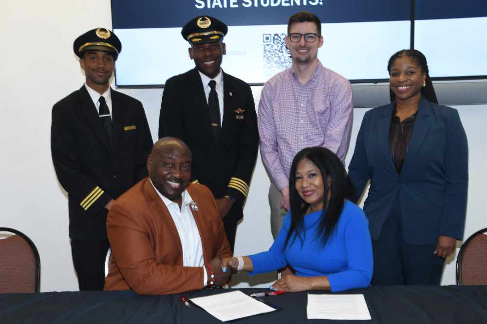 After an agreement signing between DSU and Endeavor Air, Capt. William "CJ" Charlton, Director of the University's Aviation Program, shakes hands with Robyn Murphy, Endeavor Air Senior Talent Acquisition Representative (both seated). The agreement will allow DSU aviation students to enter the airline's STEP Program, which will provide them a path to become Endeavor Air pilots and later possibly Delta Air Lines pilots.