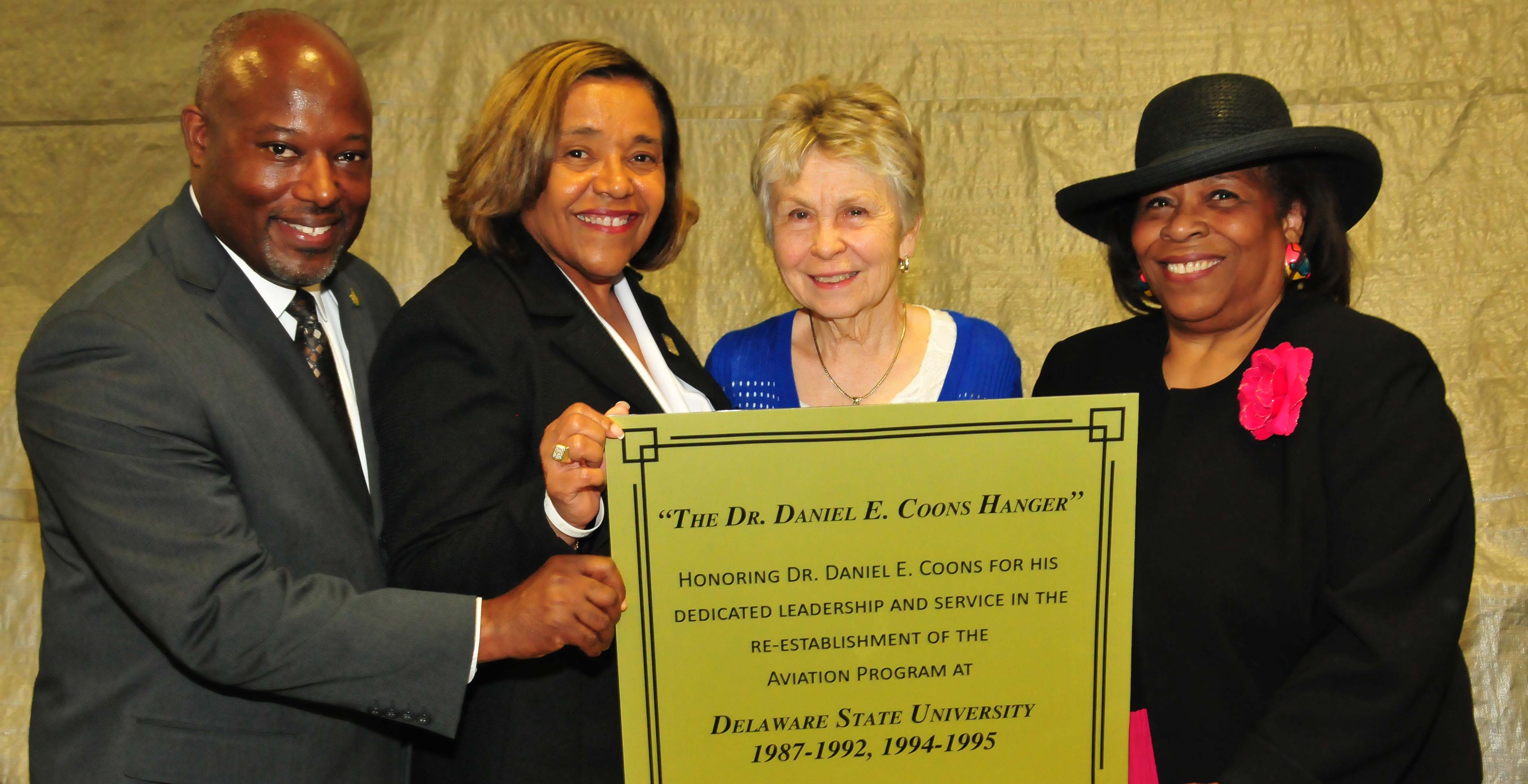 (L-r) Lt. Col. Michael Hales, director of the DSU Aviation Program; College of Business Dean Donna Covington; JoAnn Coons, widow of Dr. Coons; Dr. Wilma Mishoe, DSU Board of Trustees member, hold a copy of the plaque that is being created for the Daniel E. Coons Hangar.